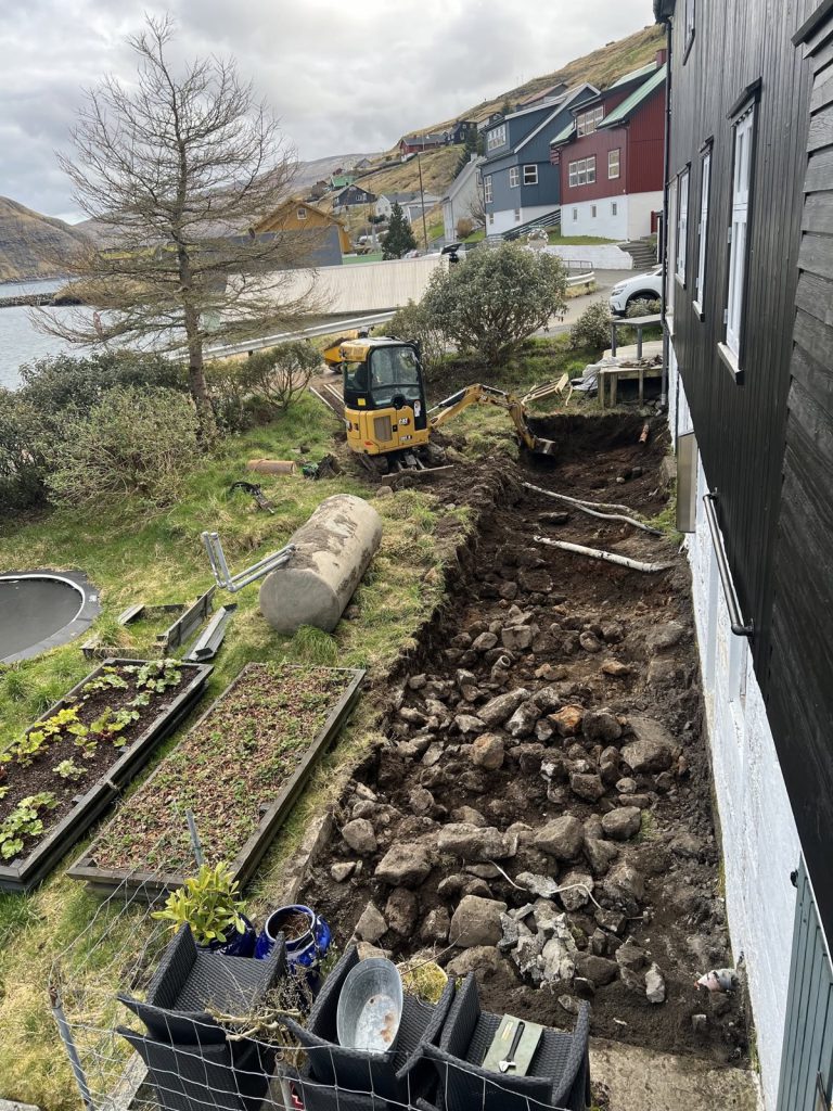 Dreneringsgrøv grivin meðfram einum húsi, við lítlari gravmaskinu longri niðri í garðinum